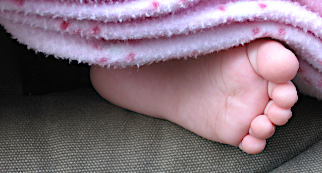 Foto: Kinderfuss unter einer hellrosa farbenden Decke